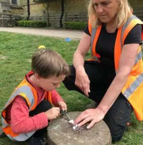Child tries to create a spark to light a fire under the watchful eye of practitioner