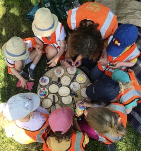 Children in a circle around a table with tree cookies being decorated in the middle